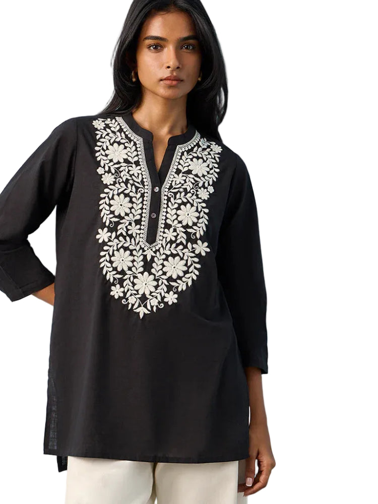Woman wearing a black embroidered top against a light blue background